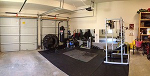 Garage Gym Equipment Neatly Set Up With Enough Room For The Car And The Baby Stroller.