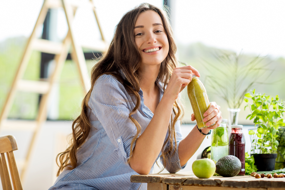 Beautiful vegan woman sitting with drinks and healthy green food at home