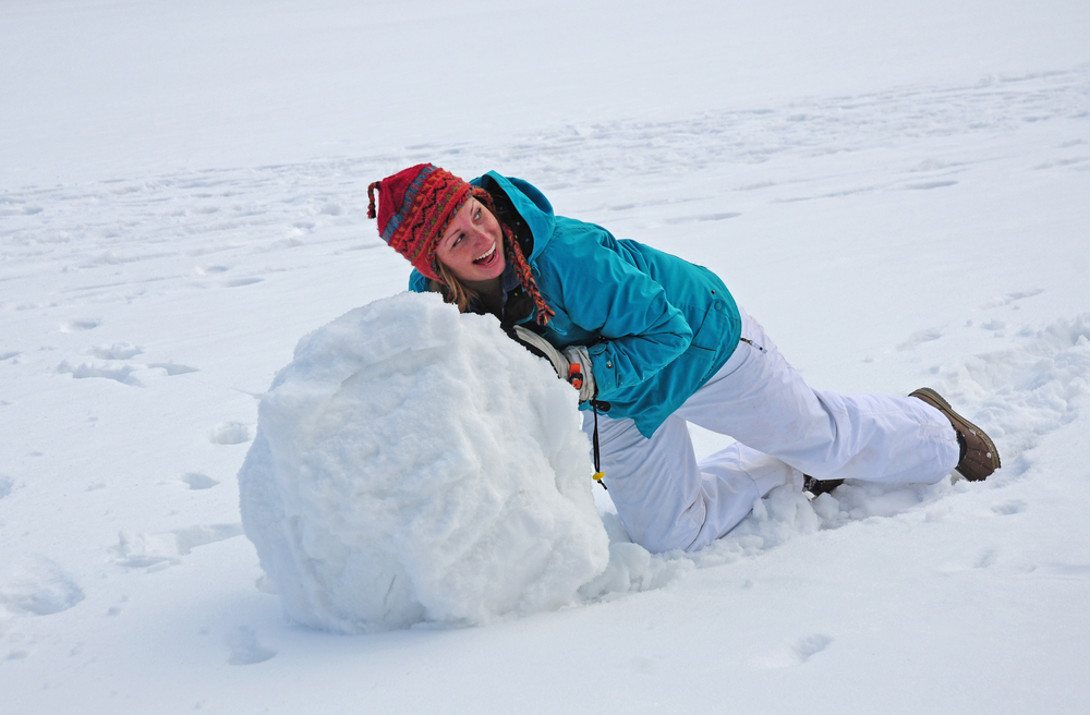 woman rolling up a giant snowball in the winter and laughing